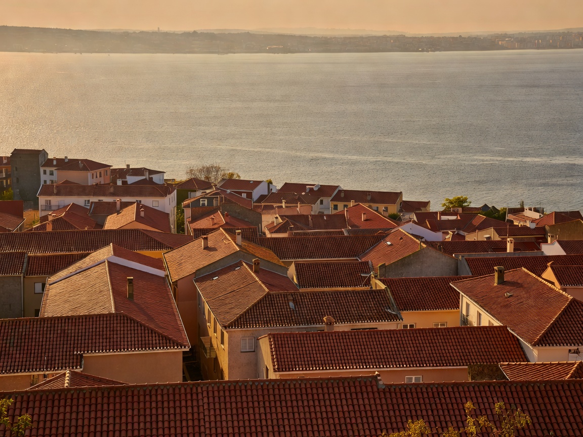 Terracotta rooftops stepping down to the wide Tagus estuary under low sun